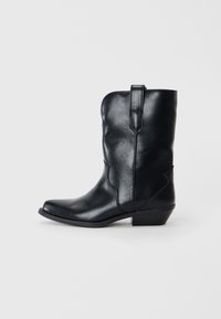 Stivale da cowboy in pelle nera con punta affusolata, altezza a metà polpaccio, cuciture decorative e tacco basso. Presenta una linguetta per indossarlo facilmente.