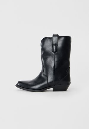 Stivale da cowboy in pelle nera con punta affusolata, altezza a metà polpaccio, cuciture decorative e tacco basso. Presenta una linguetta per indossarlo facilmente.