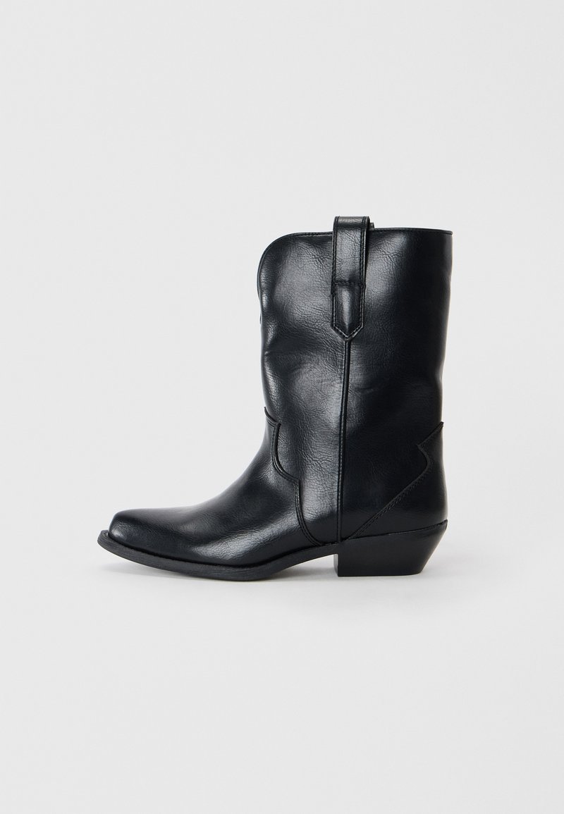 Stivale da cowboy in pelle nera con punta affusolata, altezza a metà polpaccio, cuciture decorative e tacco basso. Presenta una linguetta per indossarlo facilmente.