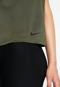 Top Nike verde oliva con diseño cropped, que presenta un logo negro en el dobladillo, combinado con leggings negros ajustados. Textura suave.
