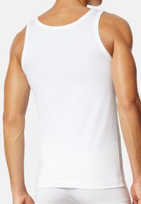 Weißes Baumwoll-Tanktop mit taillierter Passform, breiten Trägern und glatter Textur, mit einem schlichten Rücken und ohne sichtbare Muster.