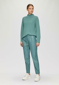 Teal geribbelde trui met hoge hals, gecombineerd met teal neplederen joggers met een elastische tailleband en koord, witte sneakers.