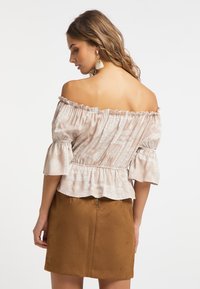 Blusa beige off-the-shoulder con motivo floreale, bordi arricciati e maniche corte. Abbinata a una mini gonna in suede marrone.