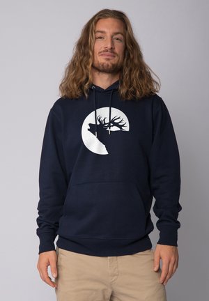 Sweat à capuche bleu marine en coton, arborant un grand graphisme blanc représentant la silhouette d'un cerf dans un design circulaire. Poche kangourou à l'avant.