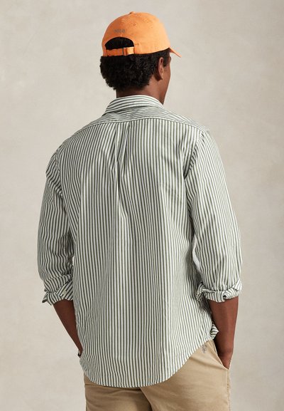 Πουκάμισο με κατακόρυφες πράσινες και λευκές ρίγες, κουμπιά μπροστά, μανίκια γυρισμένα και κυρτή τελειώματα. Πορτοκαλί καπέλο με λογότυπο "POLO". Κανονική εφαρμογή και ελαφρύ ύφασμα.