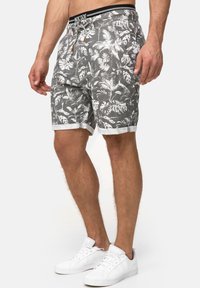 Pantalones cortos grises con patrón de hojas blancas, cinturilla elástica y cordón. Presentan dobladillos enrollados y una tela ligera. Se llevan con zapatillas blancas.