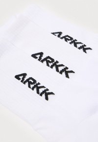 Baltos medvilninės kojinės su raibyto rinkinio tekstūra ir juodu „ARKK“ logotipu siuvinėtu šonuose. Tris poras rodomos persidengiančios.