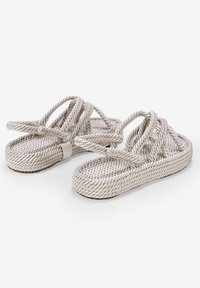 Sandales en corde de couleur beige clair avec des lanières entrelacées et une semelle texturée. Le design présente des accents noués et un semelle plate.