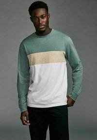 Langsleeve t-shirt met een mintgroen bovenstuk, een lichtbeige horizontale streep en een witte onderzijde; casual fit en zachte stof.