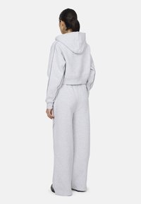 Przycięta szara bluza z kapturem, zestawiona z szerokimi szarymi spodniami dresowymi. Oba elementy mają elastyczne bandy i szwy boczne. Materiał wydaje się miękki i fakturowany.