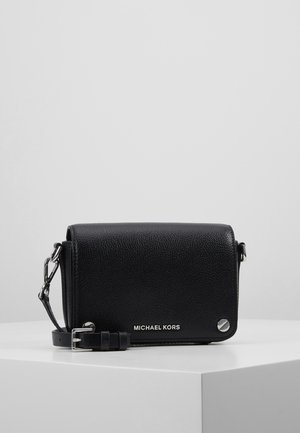 Sort tekstureret læder Michael Kors crossbody taske med sølv hardware og justerbar rem liggende på en hvid overflade.