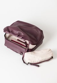 Borsa in pelle viola con un'esterno texturizzato, aperta per mostrare un interno beige a motivo e una pochette coordinata accanto.