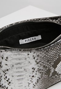 Schwarz-weiße Schlange-Print Clutch mit Reißverschluss. Das Innere besteht aus schwarzem Stoff; Markenlabel ist innen sichtbar. Strukturiertes Oberflächendesign.