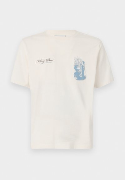 T-shirt en coton crème à manches courtes, avec un imprimé graphique bleu sur le devant et le texte "Filling Pieces". Design classique à col rond.