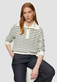 Sweter w paski w kolorze kremowym i czarnym, z kołnierzykiem i detalami z guzikami. Dziane wykończenie, w połączeniu z ciemnoniebieskimi spodniami dżinsowymi.