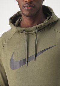 Sudadera verde oliva hecha de tela suave, con un gran logotipo negro de Nike. Equipado con cordones y una capucha texturizada.