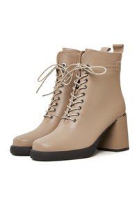 Bottines beiges à lacets avec talons carrés épais et semelles en caoutchouc noir, avec languettes latérales et œillets métalliques.