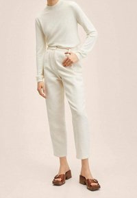 Maglietta bianca a maniche lunghe con scollatura rotonda abbinata a pantaloni cremosi e testurizzati. Sandali con plateau marroni e design a strappo completano l'outfit.