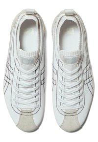 White sneakers with a smooth leather upper, contrasting black stitching, and a beige suede toe. Features a logo tag on the tongue and laces.