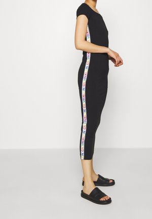 Tuta nera con design aderente, maniche corte e strisce colorate con il logo Calvin Klein sui lati; abbinata a sandali neri a scivolo.