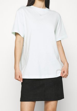 Frau trägt ein übergroßes weißes Nike-T-Shirt und einen schwarzen Rock, hält den Saum des T-Shirts mit beiden Händen.
