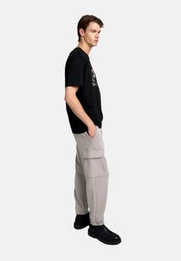 Camiseta de algodón negra con estampado gráfico, combinada con pantalones cargo gris claro con bolsillos laterales y puños elásticos, complementados con botas negras.