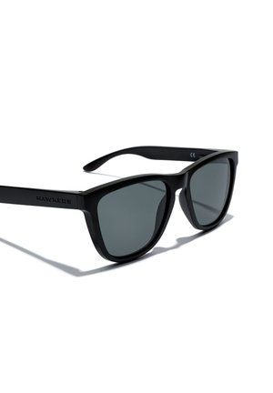 Black plastic sunglasses with gray lenses, featuring a classic square design. The arms have a matte finish and the brand "HAWKERS" embossed on one side.
