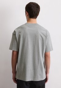 Szara bawełniana koszulka z krótkim rękawem, okrągłym dekoltem i luźnym krojem. Gładka faktura, bez widocznych wzorów ani akcentów.