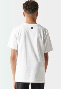 Camiseta de algodón blanca con mangas cortas, cuello redondo y un pequeño logo negro impreso en la parte superior de la espalda. Textura suave, ajuste estándar.
