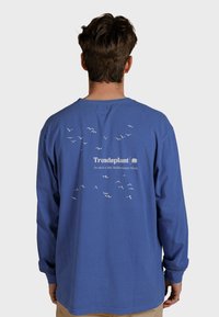 Dlouhý rukáv modré tričko s bílými siluetami ptáků a logem "Trendsplant" na zadní straně; materiál z bavlny; volný střih s kulatým výstřihem.