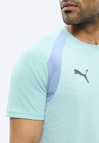 Άνδρας που φοράει ανοιχτό μπλε αθλητική μπλούζα Puma με κοντά μανίκια και διακριτικά γεωμετρικά σχέδια στο ύφασμα.