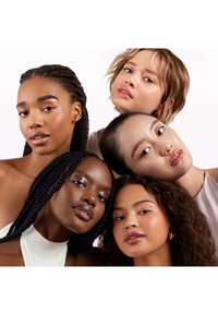 Cinq femmes aux coiffures et teints de peau variés, vêtues de tenues dans des tons neutres, affichent une peau lisse et un maquillage subtil sur fond clair.
