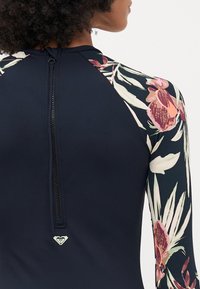 Navy rash guard with floral-patterned sleeves. Features a back zipper and a small logo at the hem. Made from stretchy, water-resistant material.