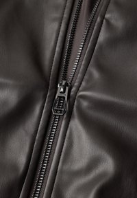 Gros plan d'une veste en cuir noire partiellement zippée montrant le curseur et les dents métalliques de la fermeture éclair.