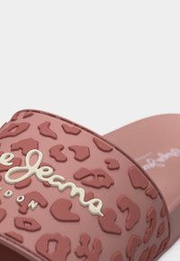 Roosa libisev sandaal, millel on reljeefne leopardimustriline tekstuur ja rihmal valge käsitsi kirjutatud kaubamärgi logo.