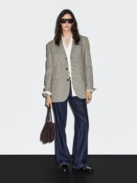 Blazer a quadri oversize, camicia bianca, pantaloni flare in denim scuro, mocassini neri e borsa in suede marrone. Gli occhiali da sole completano l'outfit.