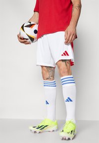 Adidas futbolo uniforma su raudona viršutine dalimi, baltais šortais. Savybėms priklauso mėlynos juostos ant kojinių, ryškiai žalios spaudimui skirtos sportbačiai ir raštuotas futbolo kamuolys.