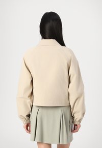 Beige cropped jack met een zachte textuur, met een knoopsluiting bij de kraag en elastische manchetten, gecombineerd met een geplooide groene rok.