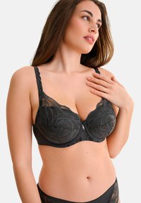 Soutien-gorge en dentelle noire avec des motifs floraux, support à armatures, bretelles réglables et fermeture à crochets sur le devant.