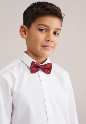 Burgundska metuljček z belimi pikami v kombinaciji s svežo belo srajco z ovratnikom, z zaponkami na sprednji strani in gladko teksturo tkanine.