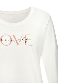 Vit långärmad skjorta med texten "Älska dig själv" i blandad typografi; mjukt tyg med rund halsringning och avslappnad passform. Inga ytterligare detaljer.
