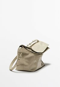 Beige leather handbag with a soft, textured surface, a flap closure, and a single adjustable strap. Features a wide, structured base.