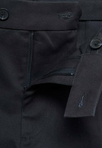 Los pantalones negros presentan un cierre de botón, cremallera y un bolsillo lateral con una textura suave y un diseño entallado. Detalles cosidos alrededor de las aberturas.