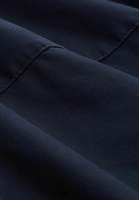 Marineblauwe stof met een gladde textuur, met zichtbare stiksels langs de randen en subtiele plooien, wat wijst op zachtheid en beweging.