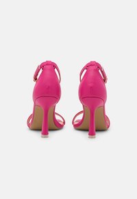 Vaaleanpunaiset synteettiset korkokengät, joissa on säädettävät nilkkahihnat, pyöristetty kärki ja hoikka, läpinäkyvä korko. Pohja vaaleanruskea.