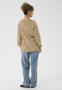 Beiges, übergroßes Sweatshirt mit langen Ärmeln und weitem Halsausschnitt, kombiniert mit hellblauen, lockeren Jeans und schwarzen Schuhen.
