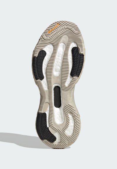 Suela de zapato con un diseño de goma texturizada en beige y negro. Presenta surcos y secciones acolchadas para mejorar el agarre y la comodidad.