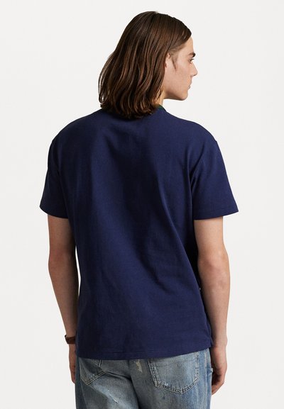 Tamsiai mėlynas medvilninis marškinėlis trumpomis rankovėmis, apvalia iškirpte ir vientisa tekstūra. Dėvimas su nuvytusiomis mėlynomis džinsinėmis kelnėmis, rodančiomis laisvalaikio stilių.