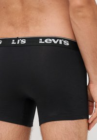 Fekete göndör pamut boxer alsónadrág fekete gumírozott derékkal, amelyen fehér "Levi's" márkázás található. A szabása kényelmes és modern.