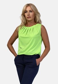 Neon zielony top bez rękawów z plisami przy dekolcie. Zestawiony z ciemnogranatowymi, teksturowanymi spodniami z wzorem kropeczek.